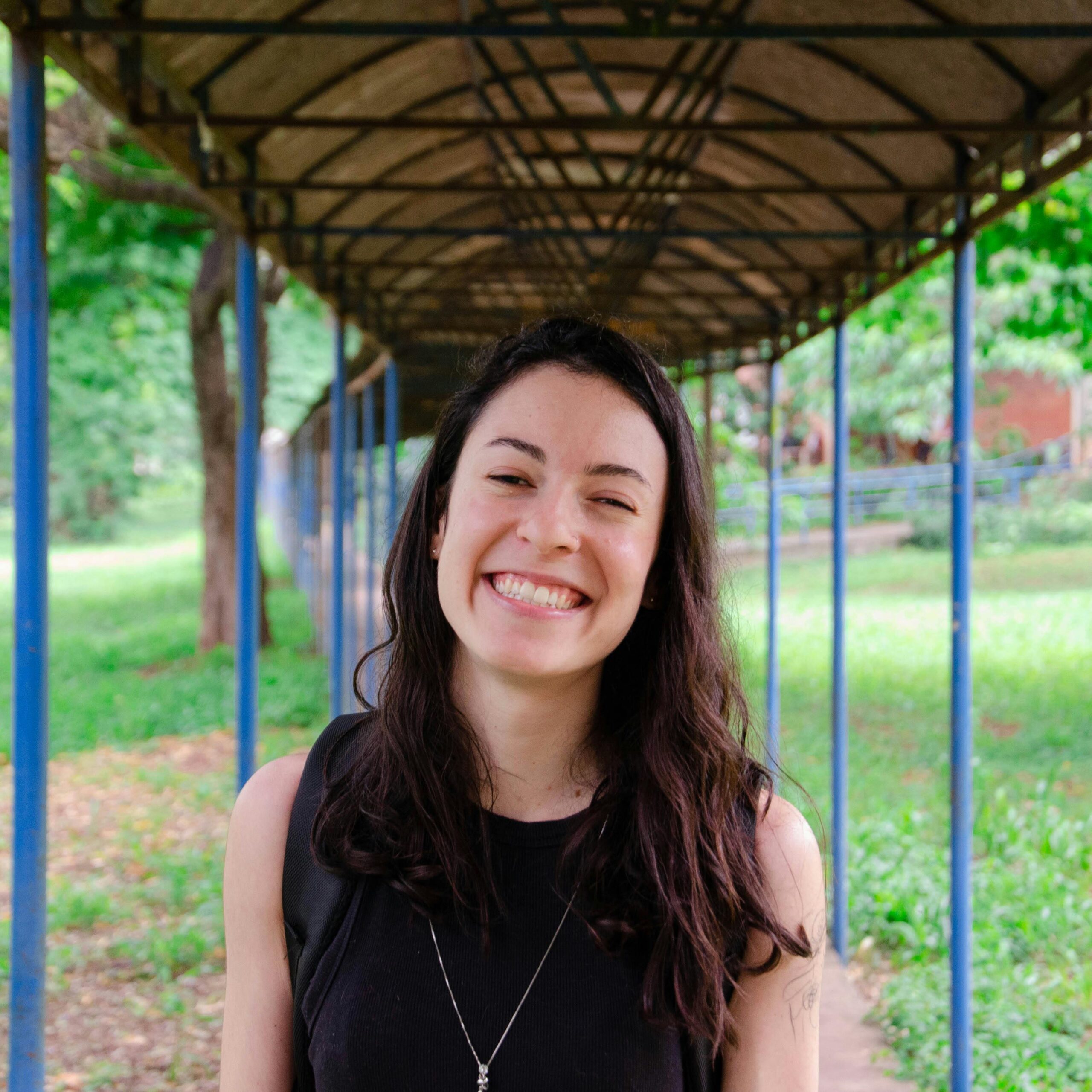 Portrait of a woman smiling under a canopy in a lush outdoor park.