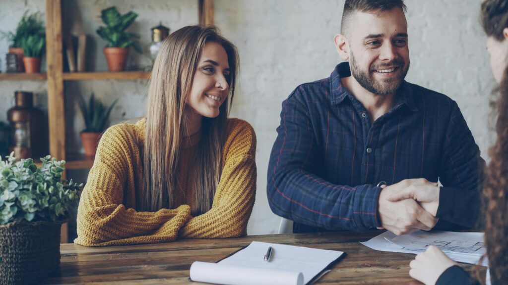 Couple securing a deal with handshake, smiling in a casual setting.
