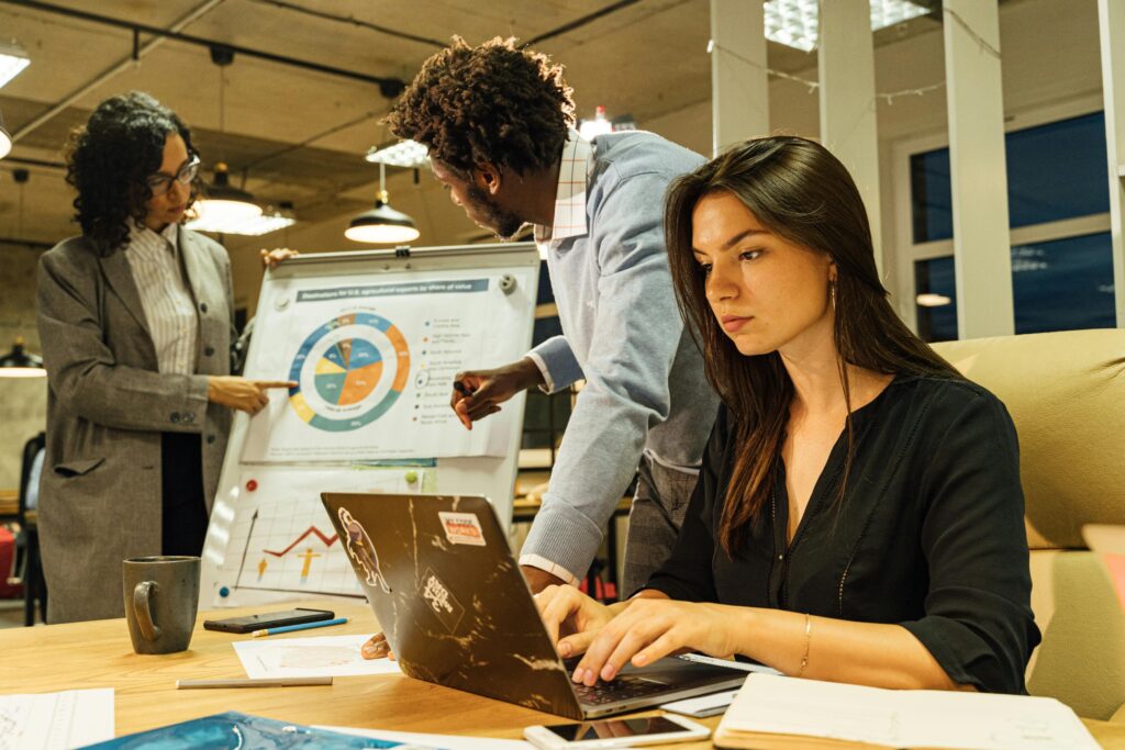 Professional team collaborating in a modern office, analyzing business charts and data on a flipchart and laptop.