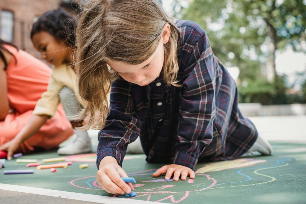 Kids creatively draw with chalk on asphalt, enjoying outdoor playtime.