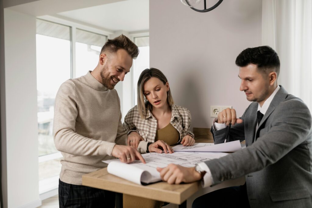 Three adults reviewing real estate blueprints indoors at a table.