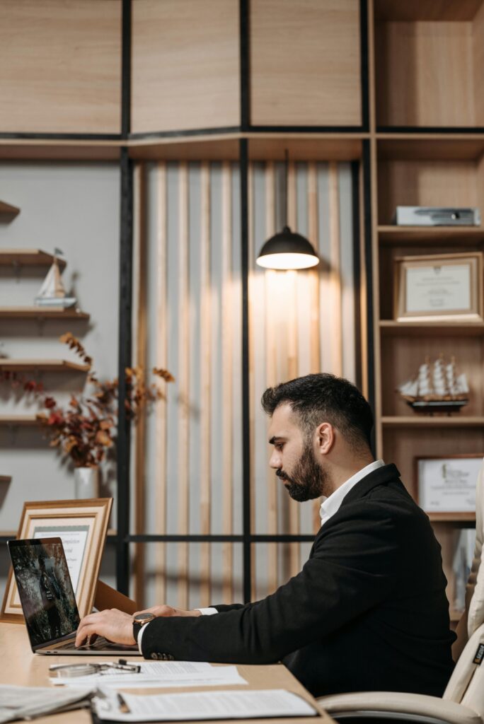 Professional businessman with beard working on laptop in a modern office space.