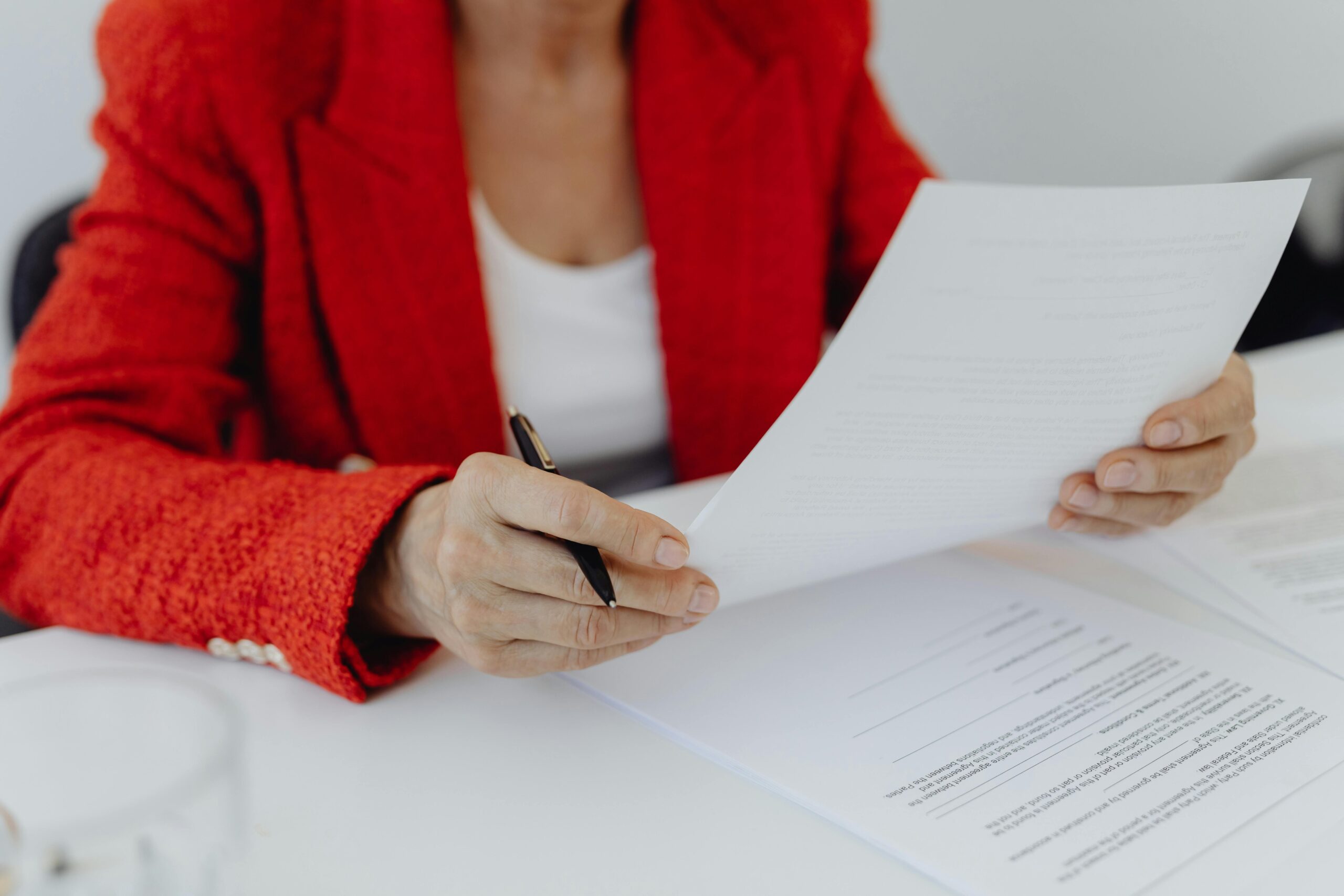 Close-up of a person in a red jacket reviewing documents with a pen in hand.