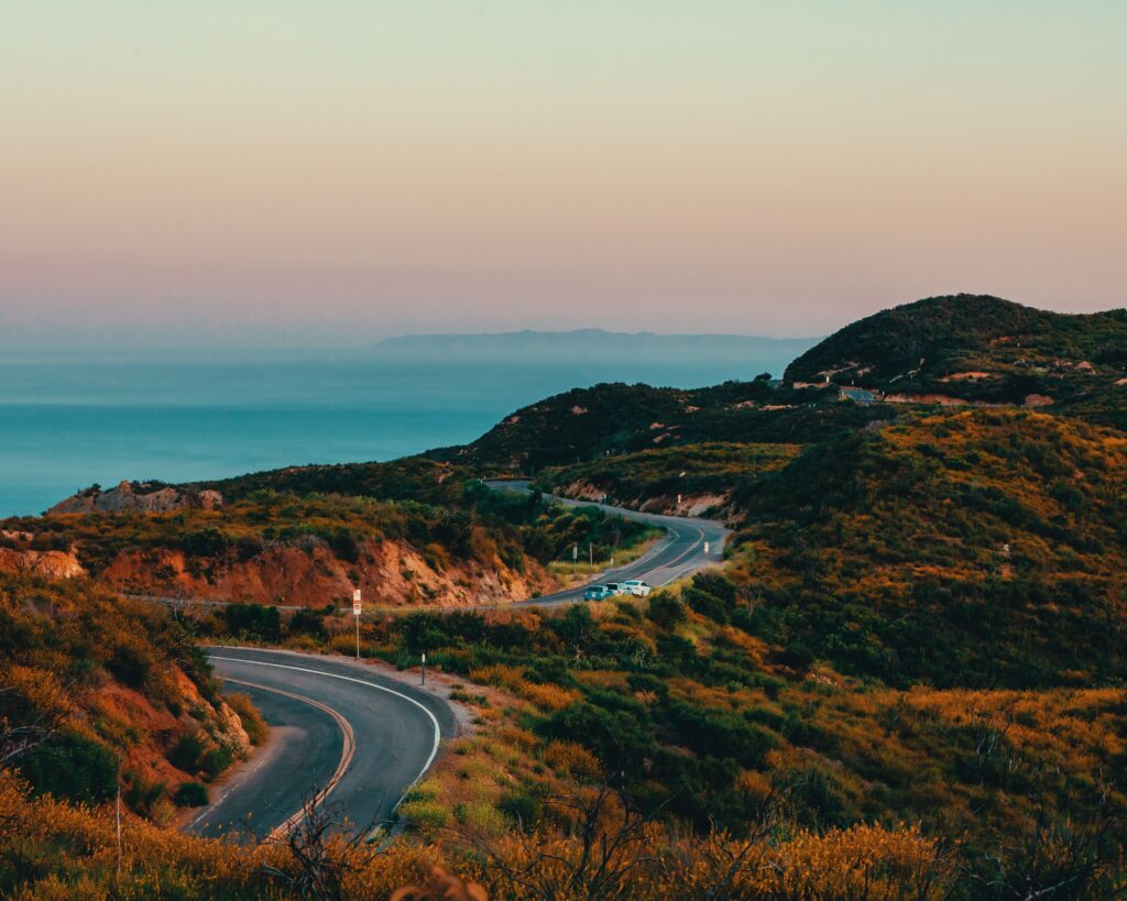 Stunning aerial view of a winding highway in Malibu with ocean and mountains at sunset.