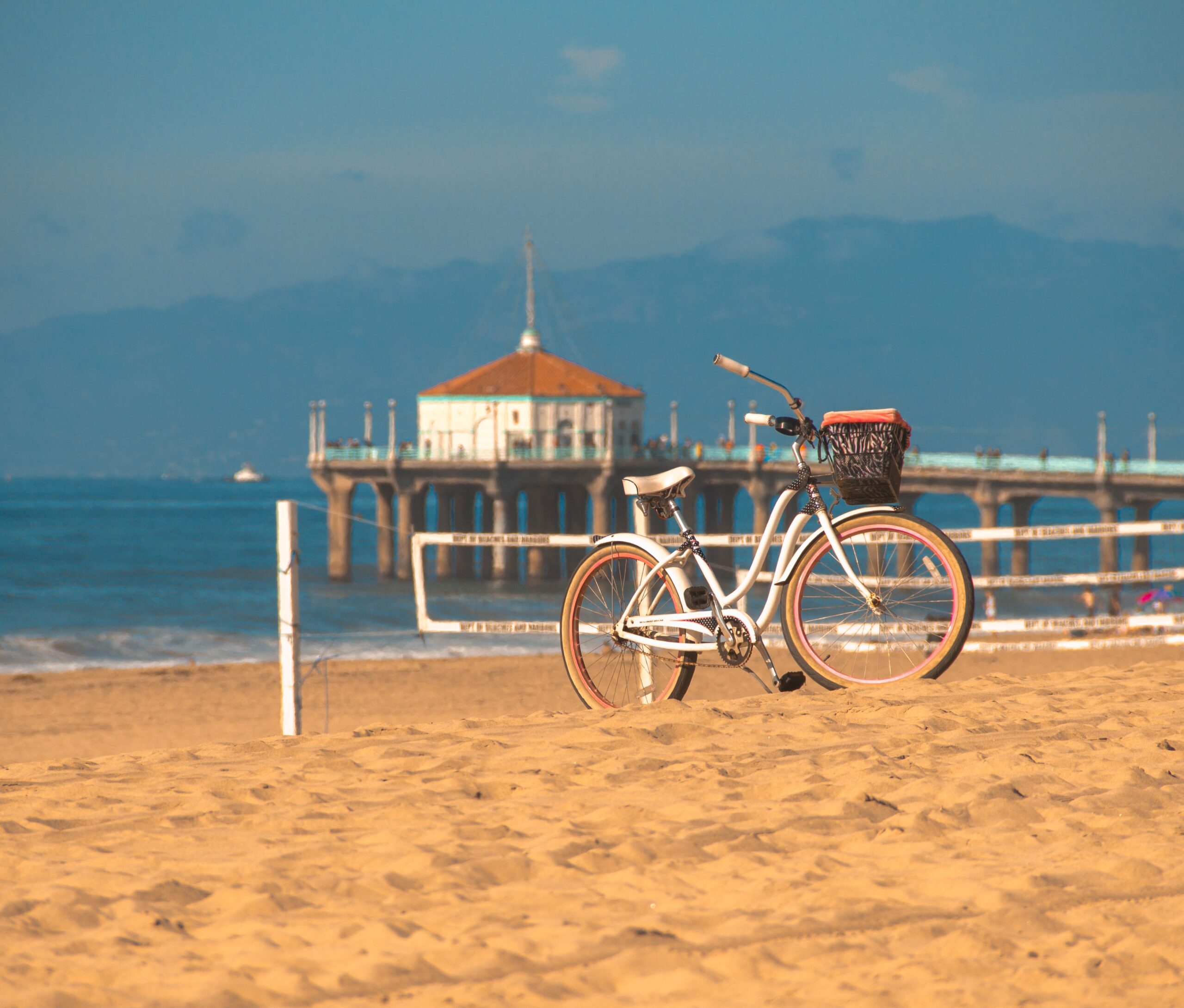 Bicycle parked on sandy shores with Manhattan Beach Pier in the background in Los Angeles, CA.