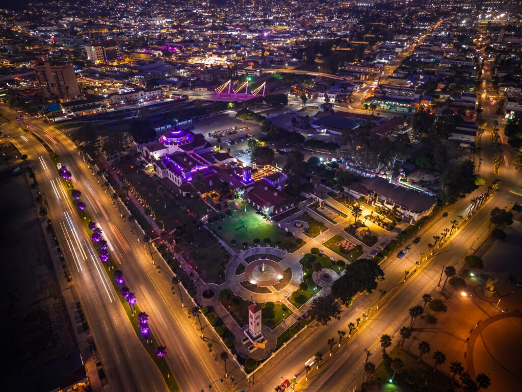 Vibrant aerial night view of Ensenada cityscape with illuminated streets and buildings.